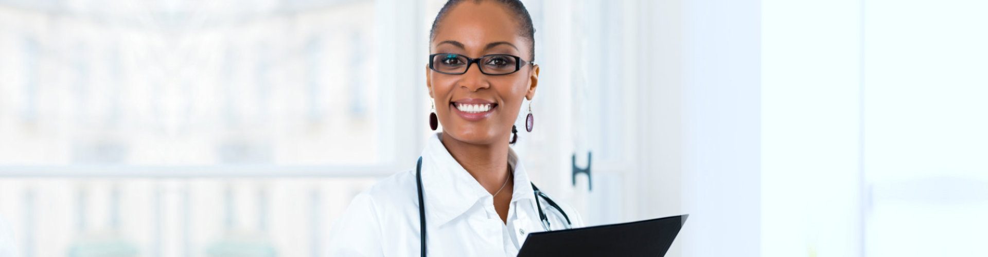 Young female black doctor standing at a window in clinic with a file or dossier